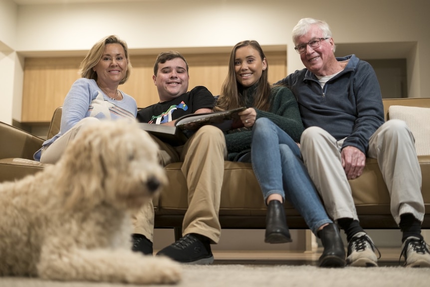 Tom Neale sits with his mum, sister and dad on the couch, with their dog in the foreground