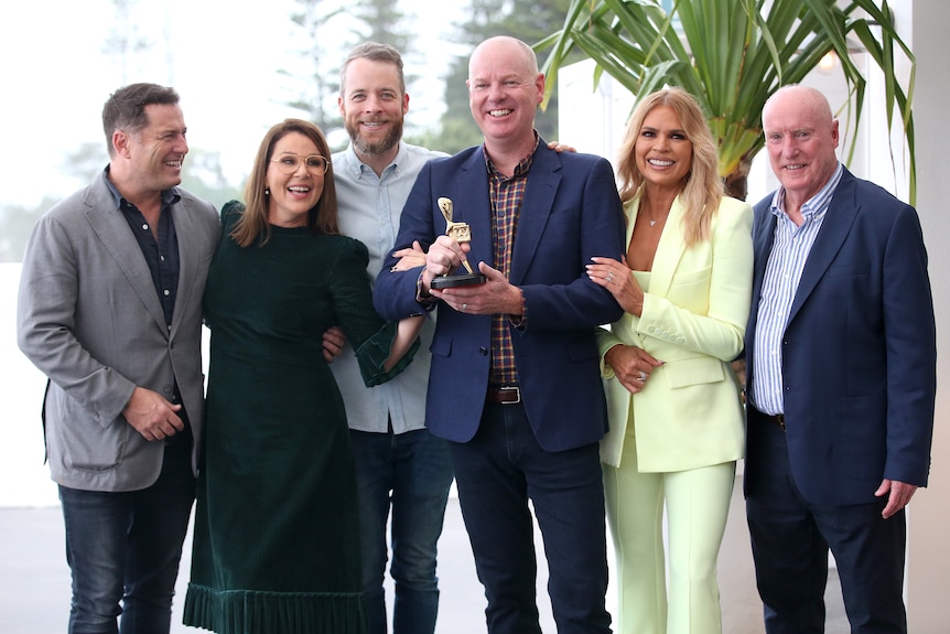 Six people standing smiling holding a small statue 