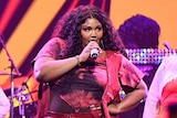 Lizzo wears a pink outfit and sings with backing dancers behind her