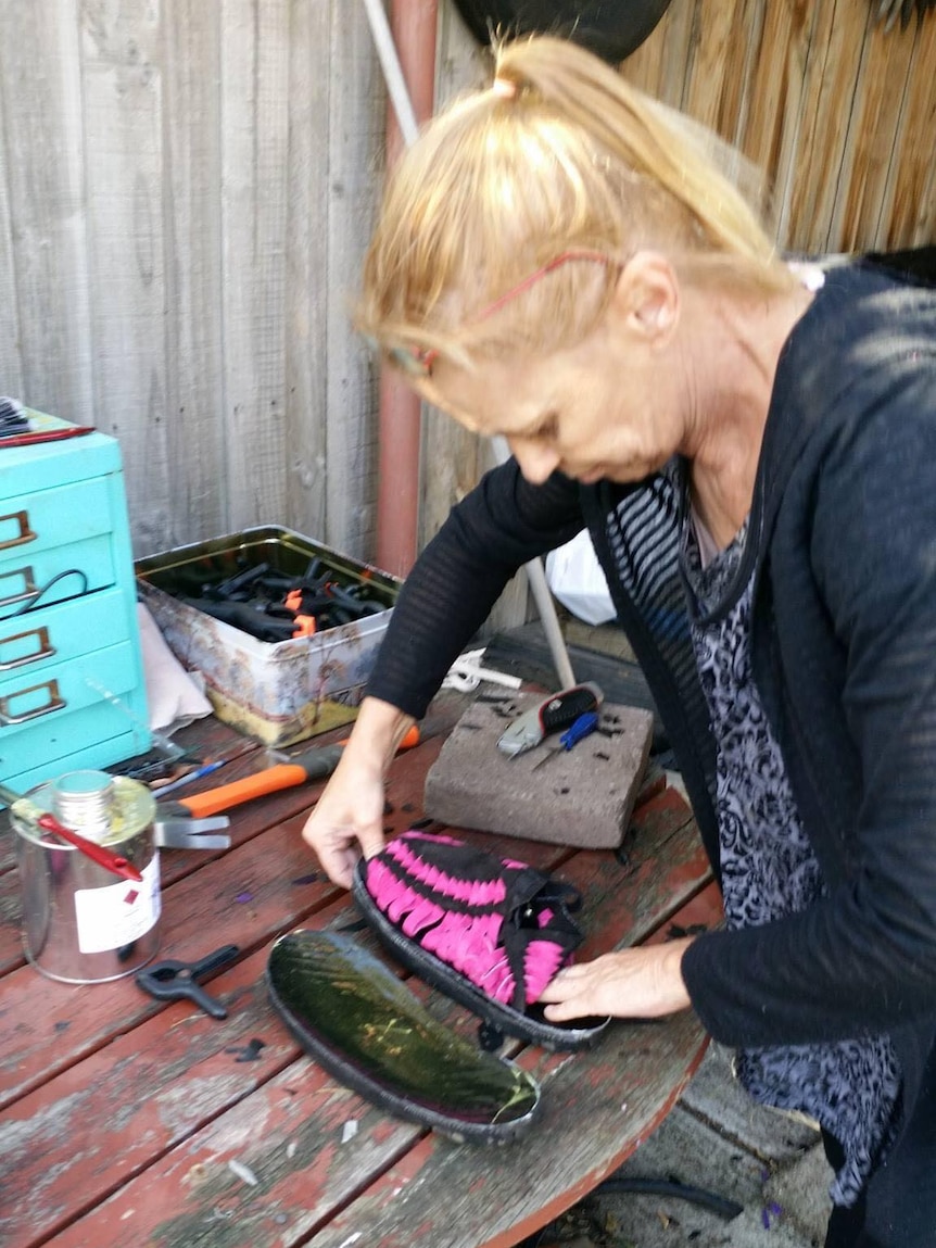 A woman presses on a pair of black and pink treads in her back yard, she is gluing the soles.