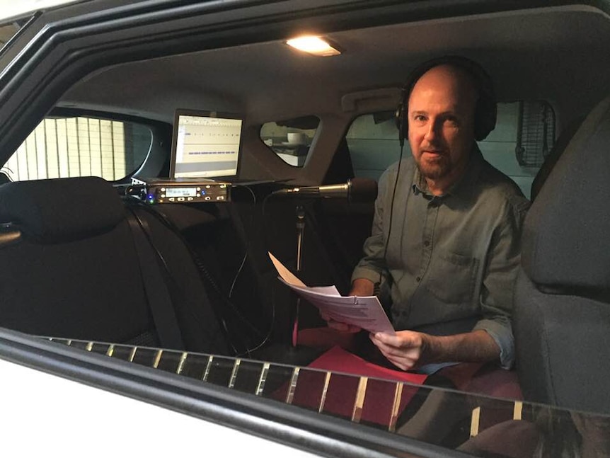 Man wearing headphones in back seat of car talking into microphone.