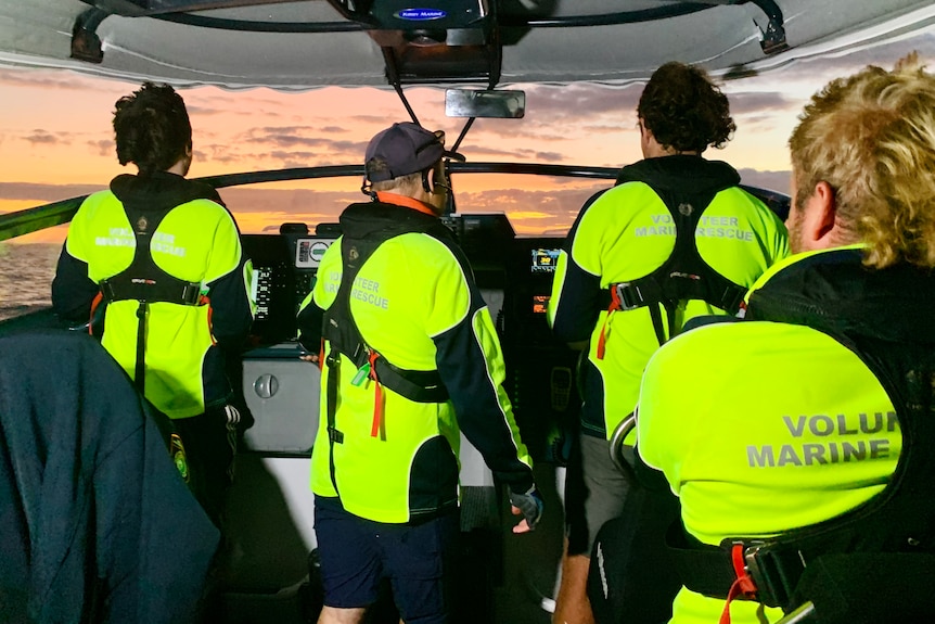 Four men stand in fluro yellow shirts on a boat with their back to the camera