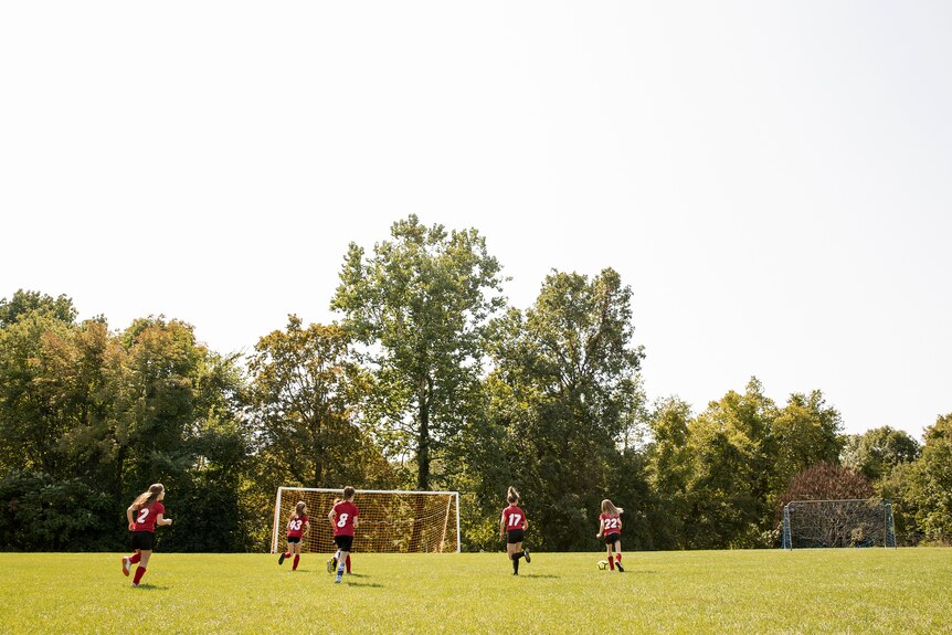 A soccer team wearing red jerseys runs towards the goal