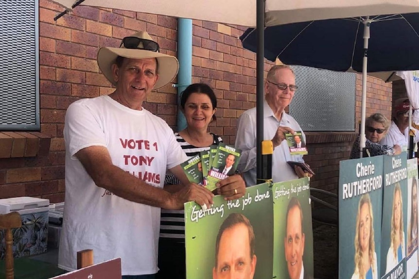 Two men and a woman stand beside a brick wall holding how to vote flyers for Tony Williams.