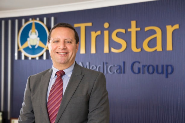 Man in suit smiles in front of Tristar Medical sign.