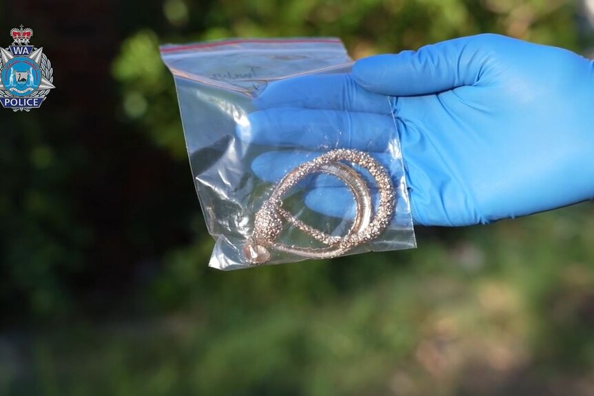A blue gloved hand hold a plastic bag containing large gold earrings.