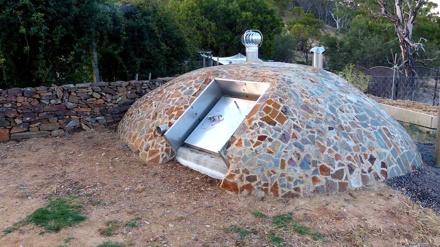 A dome structure made of stone with a metallic door set into its side with a forest in the background