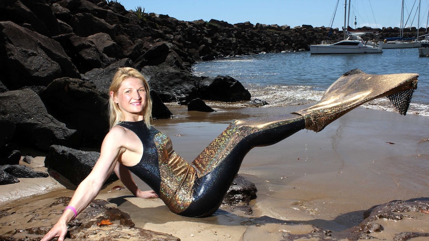 A woman shows off her black and gold sparkly mermaid outfit on the beach.