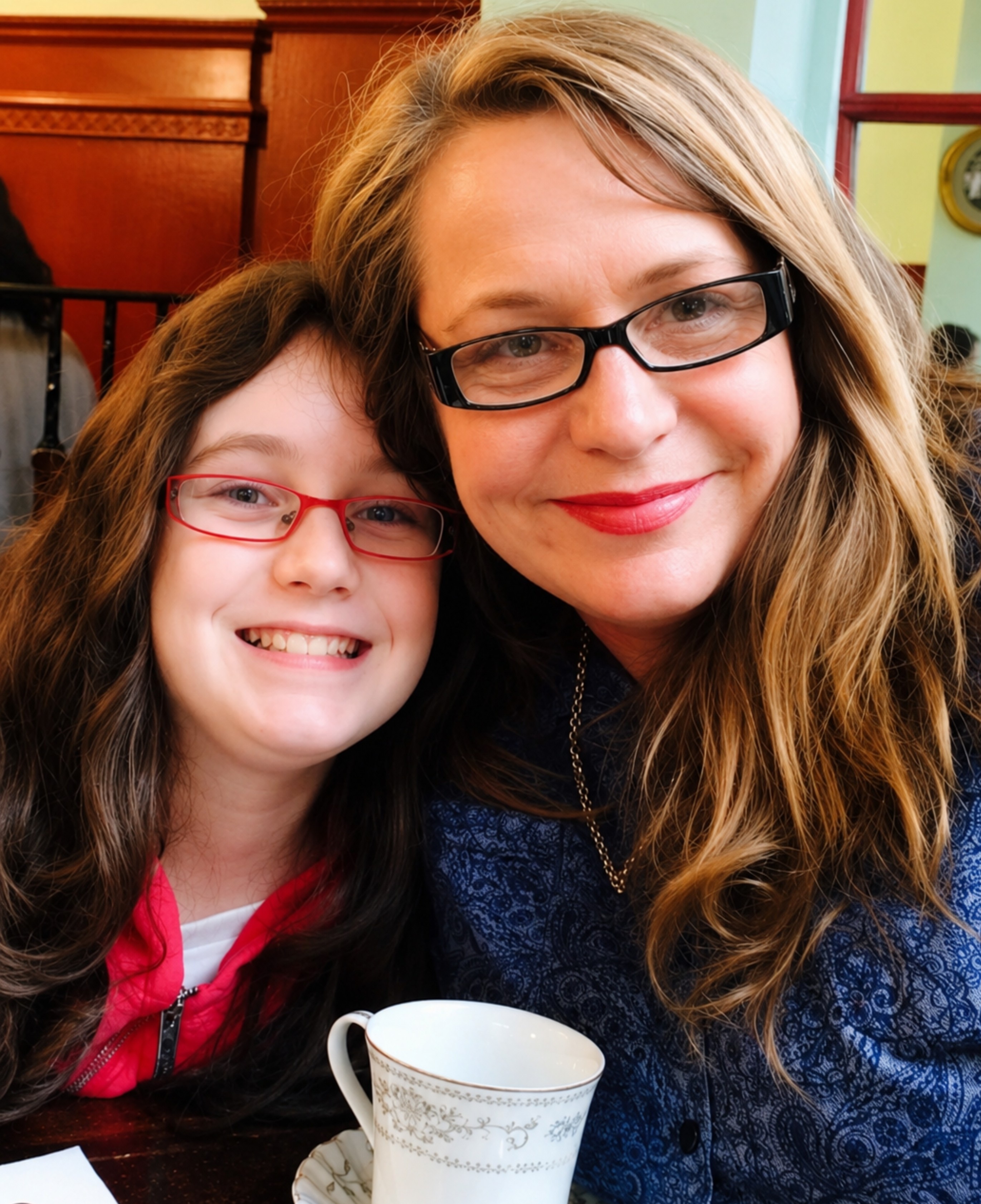 Woman in black glasses smiles closely to young girl in pink glasses