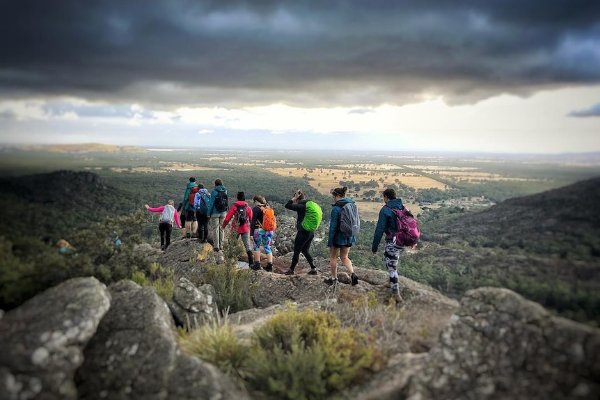 A group of women walk along the crest of a mountain under grey skies.