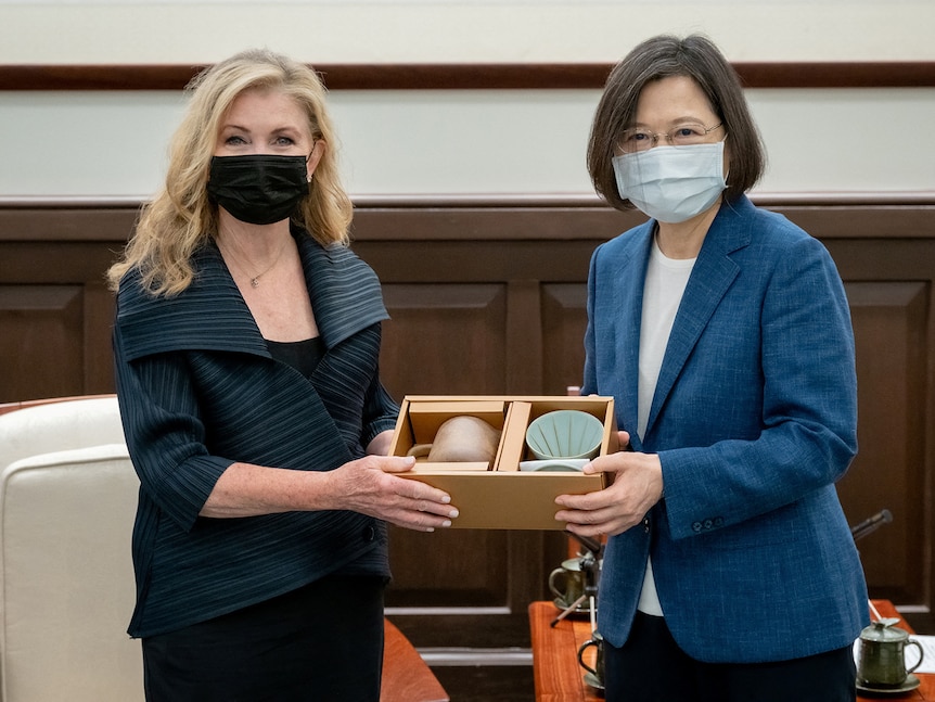 Two women wearing masks pose for the camera while holding a box between them.