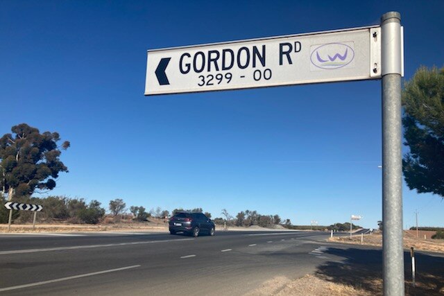 A road sign which reads Gordon Road in front of a road with a car travelling on it