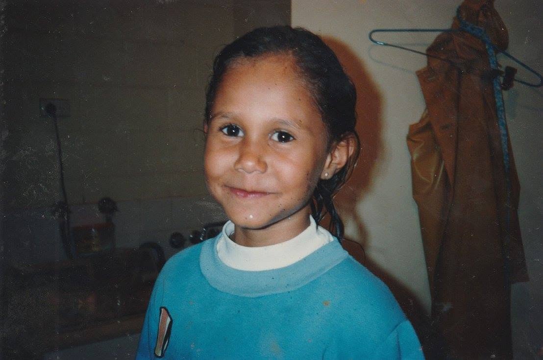 A girl with a green and pink top has a large smile on her face.