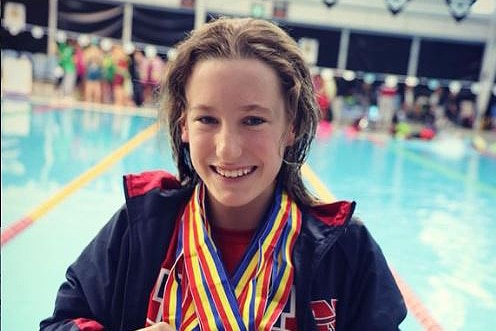 A girl in a wheelchair with medals around her neck next to a competition pool