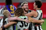 Four Collingwood AFL players embrace in a circle as they celebrate beating the West Coast Eagles.