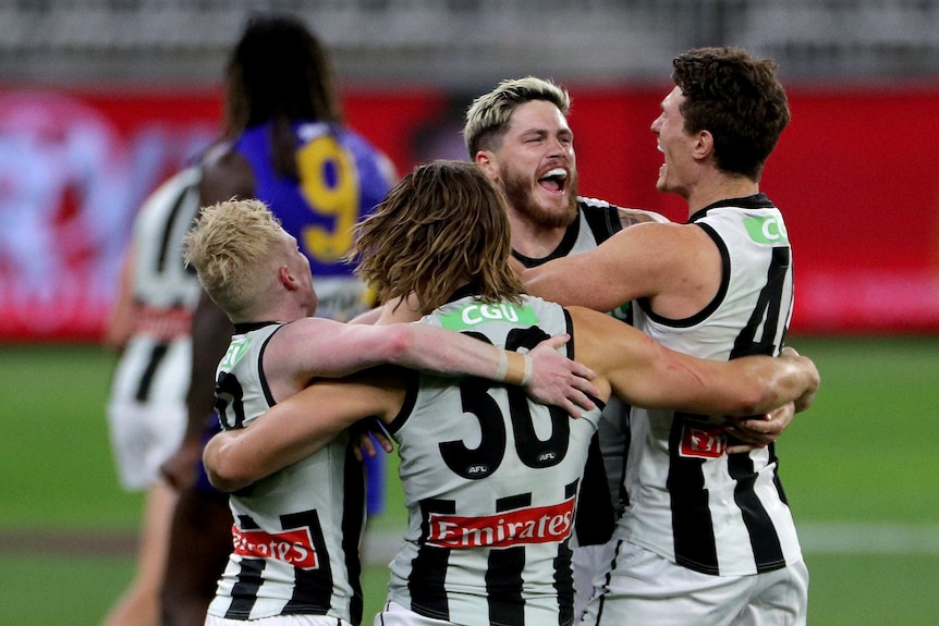 Four Collingwood AFL players embrace in a circle as they celebrate beating the West Coast Eagles.