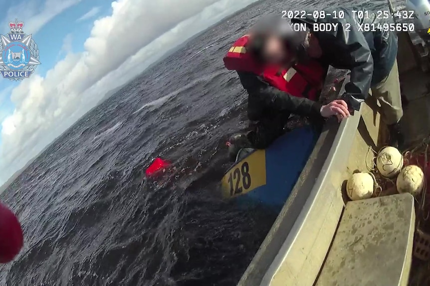 Body cam screenshot with WA police logo of man wearing a life jacket around his neck being helped into the boat from water.