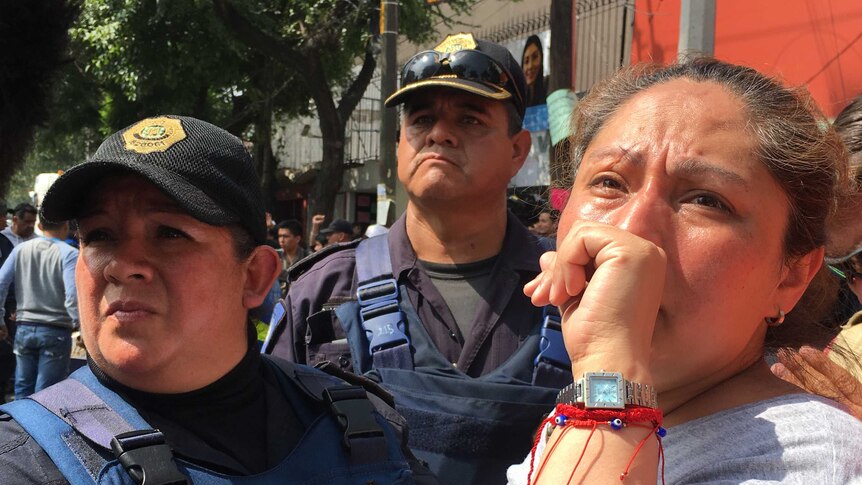 A woman cries as she stands alongside authorities at the site of the collapsed Mexico City School.