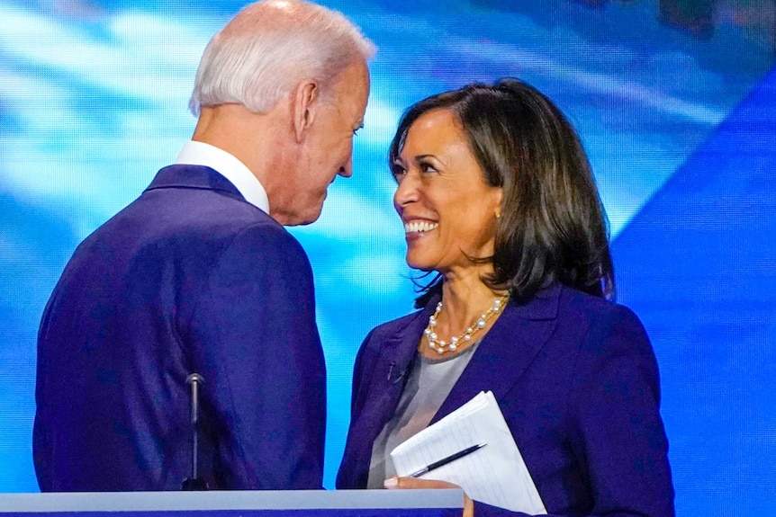 Joe Biden and Kamala Harris smile at each other while shaking hands