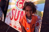 A young child stands in front of a bonnet painted with an AFL team's logo.