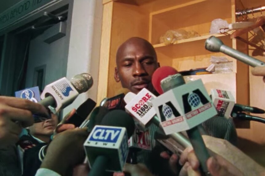 Michael Jordan is almost completely obscured by microphones during media availability in the Chicago Bulls' locker room.