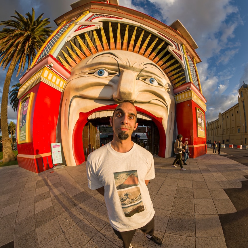 a man wearing a white shirt stands in front of Luna Park in Saint Kilda