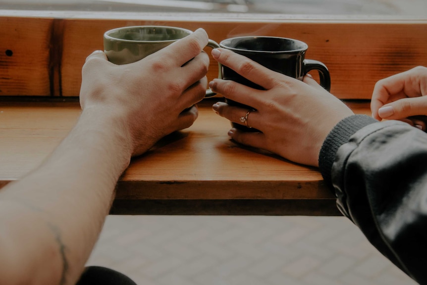 A man and a woman's hands cradle cups of steaming drinks.