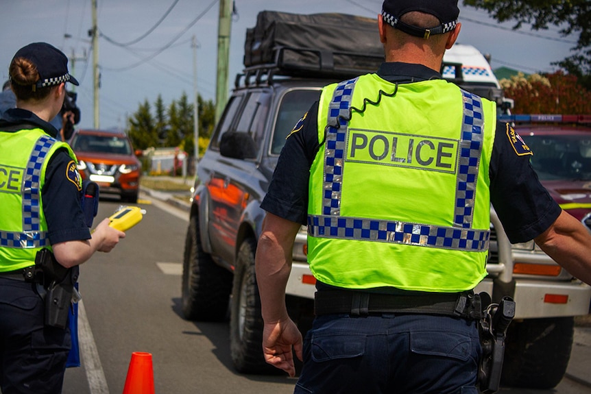 Agentes de la policía de Tasmania saludando a los vehículos en la estación de pruebas aleatorias al borde de la carretera.