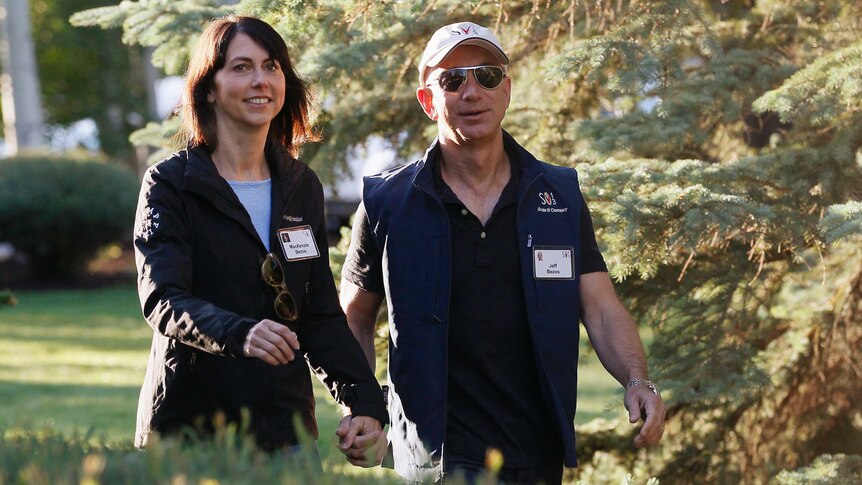 MacKenzie and Jeff Bezos walk by pine trees, wearing name tags and dressed casual clothing.