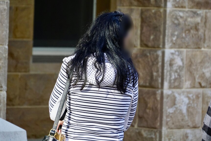 A woman wearing a black and white striped jumper stands with her back turned looking to her right.