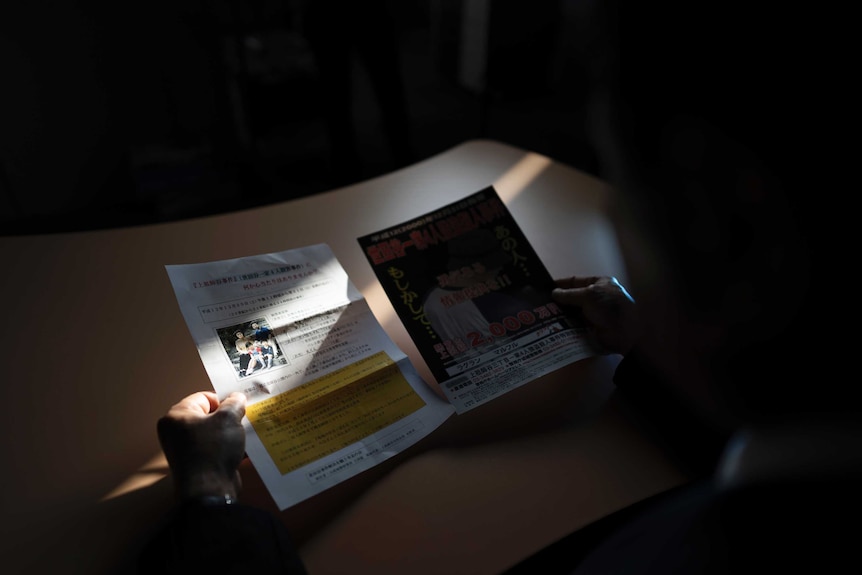 A man holding fliers in a darkened room