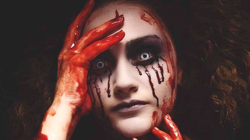 A woman in scary Halloween make-up, including blood smeared on her hands and running down her eyes and white contact lenses
