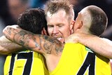 Jack Riewoldt's face can be seen as he hugs Daniel Rioli and Dustin Martin, whose backs are to camera
