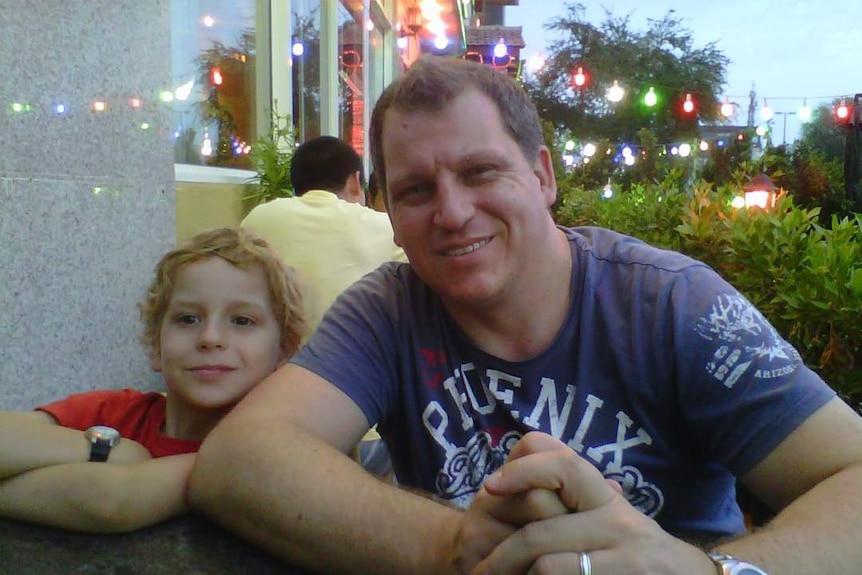 A man smiles with his son at an outdoor restaurant 