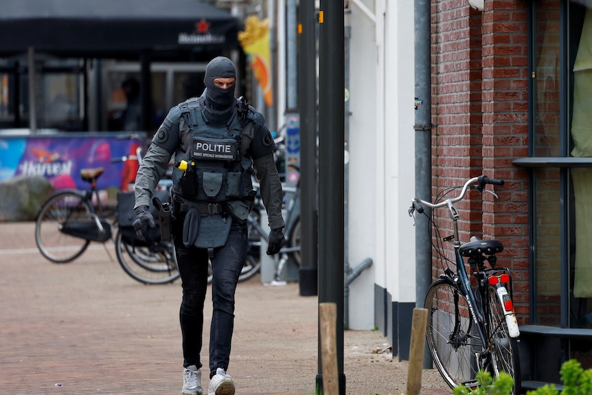 A police officer wearing heavy armour and balaclava walking in a small town