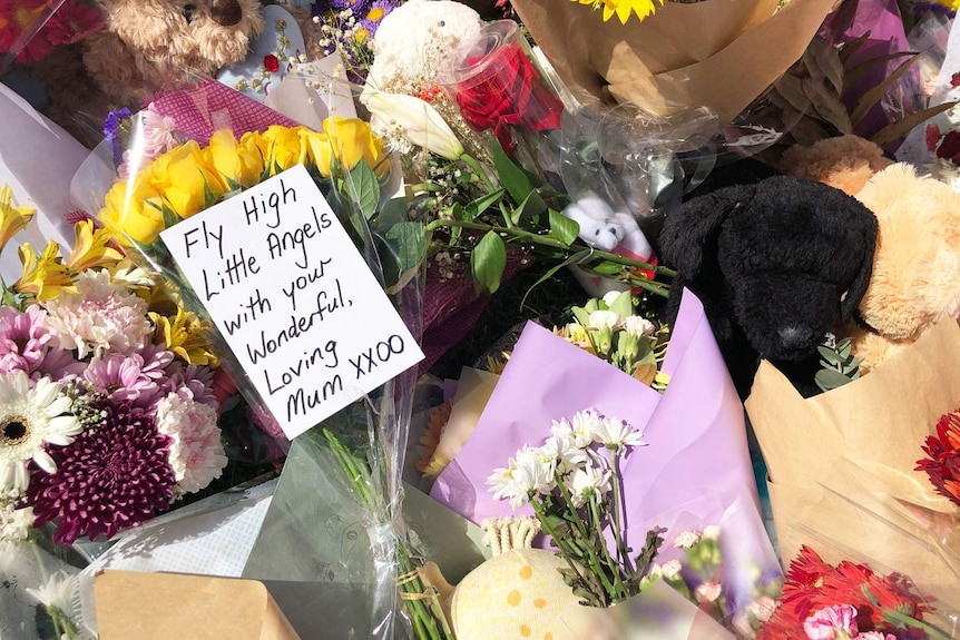 Flowers, toys and tributes with message 'Fly high little angels with your wonderful loving mum' on the street.