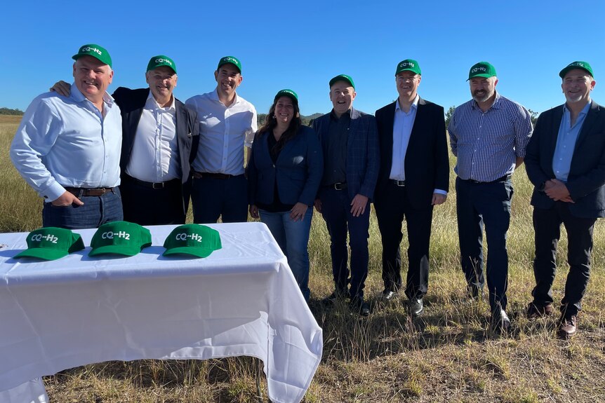 group of men and one woman stand in a paddock wearing branded hats
