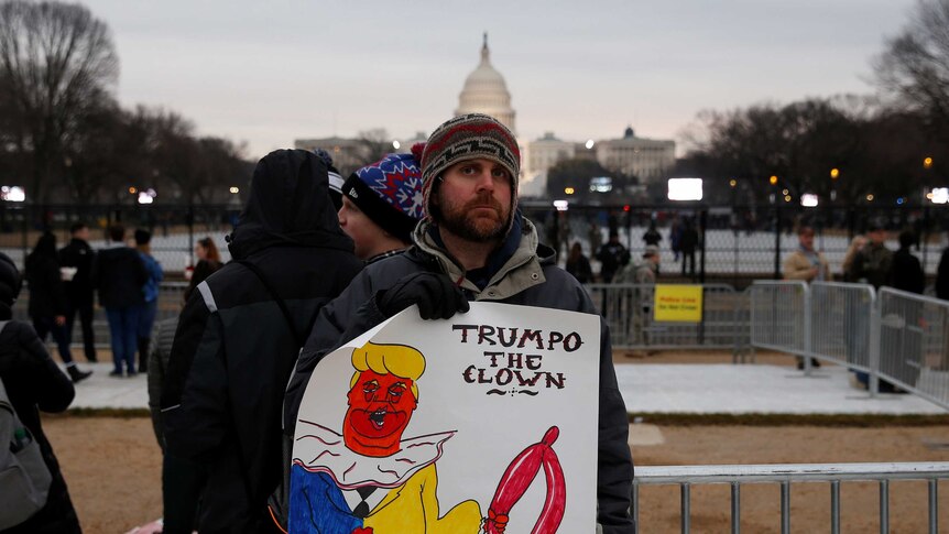 An anti-trump protester holds a sign saying "Trumpo the clown"