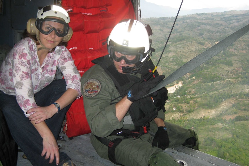 Lisa Millar wears a helmet and glasses while sitting next to military personnel while in an aircraft.