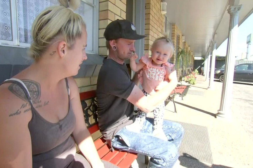 Family with a baby sitting outside motel room.