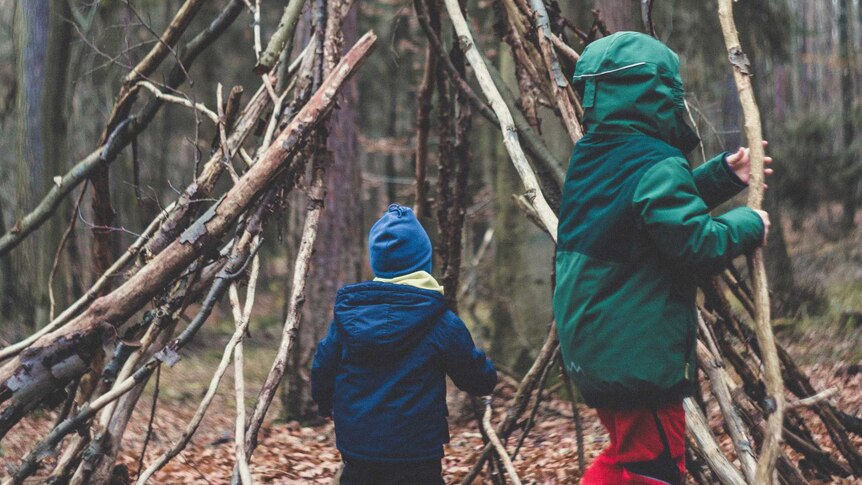 Two children are collecting fallen branches and building a cubby in a forest