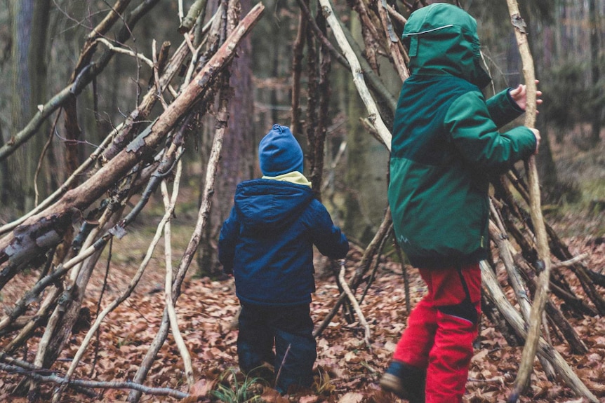 Two children are collecting fallen branches and building a cubby in a forest