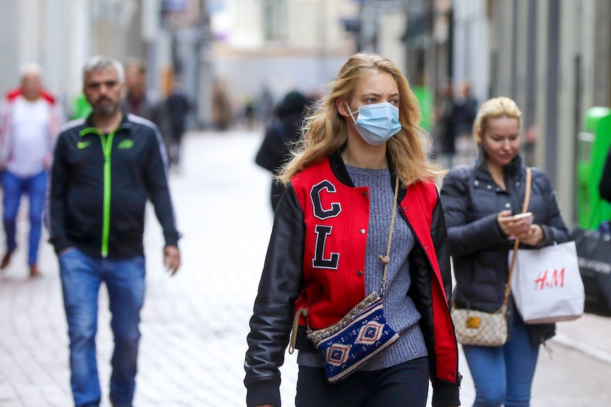 O tânără cu părul lung și blond poartă o mască chirurgicală albastră pe o stradă din Amsterdam