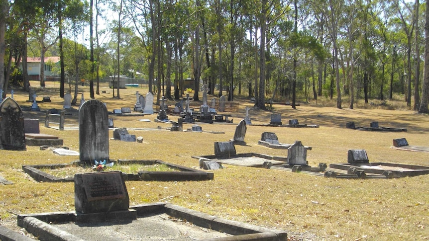 Old graves in a country cemetery with gum trees in the background, and buildings in the distance.
