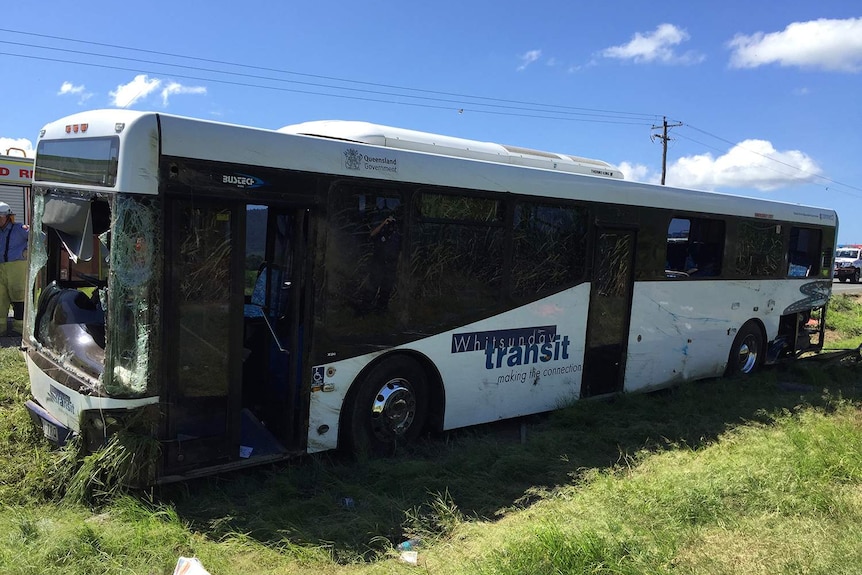 Damaged bus at scene of rollover accident with grass in foreground and road behind.