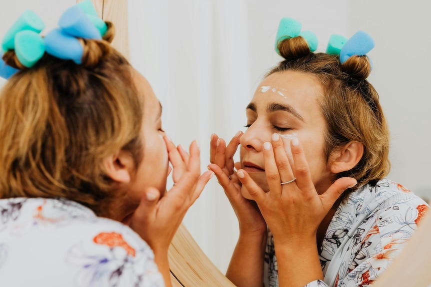A woman is putting face cream while looking into a mirror.