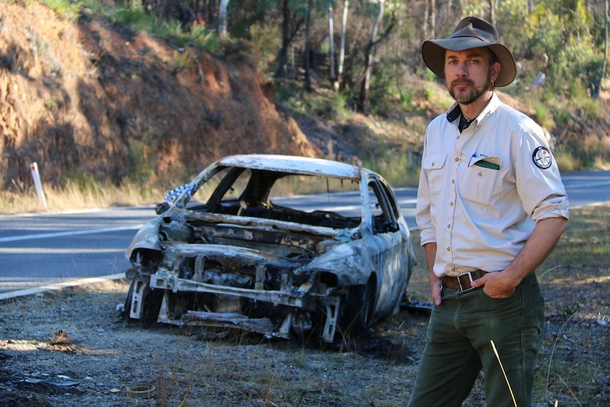 Brandon Gaplin stands in front of a burnt-out car.