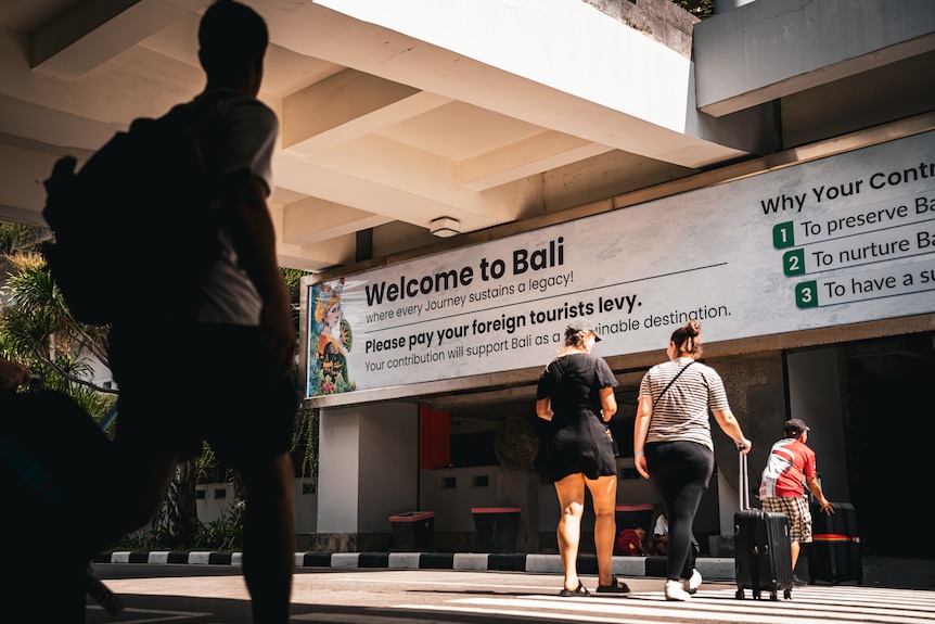 A group of people walk passed a sign that says Welcome to Bali.