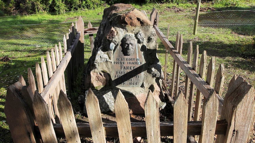 The gravestone of an Aboriginal man, surrounded by a wooden picket fence.