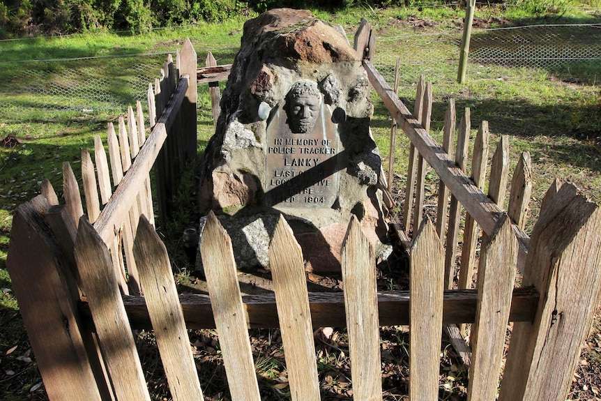 The gravestone of an Aboriginal man, surrounded by a wooden picket fence.